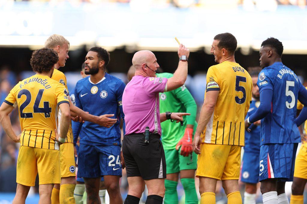Referee Simon Hooper giving a yellow card to Benoit Badiashile of Chelsea