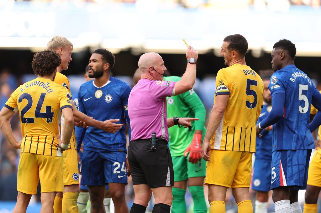 Referee Simon Hooper giving a yellow card to Benoit Badiashile of Chelsea