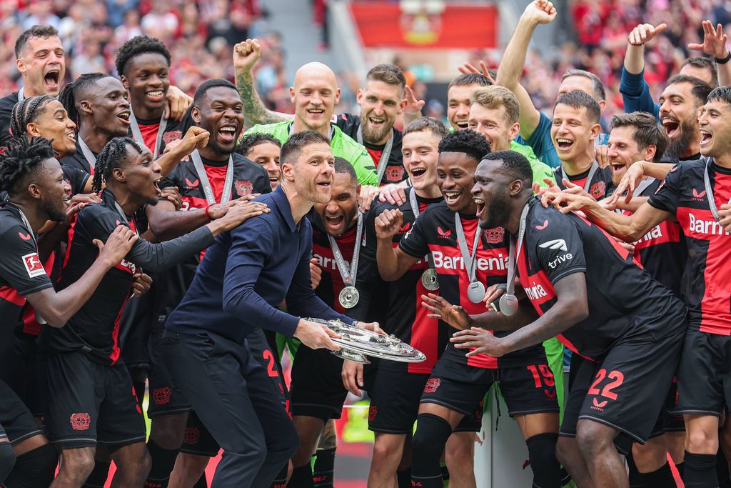 Coach Xabi Alonso Leverkusen holds the trophy, next to him Jeremie Frimpong, Victor Boniface, Florian Wirtz, Nathan Tella, and Jonathan Tah watching excitedly
